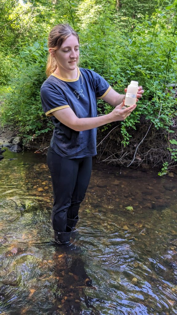 Student standing in river with a full sample collection bottle.